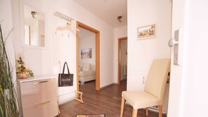 Ein Hotelzimmer mit Holzboden, einem beigefarbenen Sessel, einem Schreibtisch mit Schubladen, einem an der Wand befestigten Kleiderhaken, einem gerahmten Bild und einem floralen Teppich.