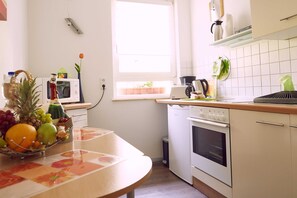 A kitchen with a microwave, oven, and sink. There is a fruit bowl on the counter and a window with blinds.