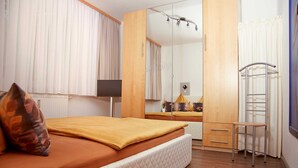 Ein Schlafzimmer mit Bett, Spiegel, Kleiderschrank, einem kleinen Tisch und einem Stuhl.