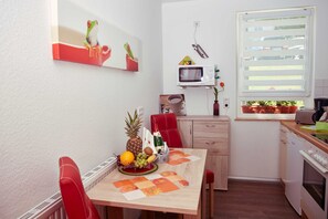 A compact kitchen with a dining table set for two, a microwave, a toaster, and a small window with blinds.