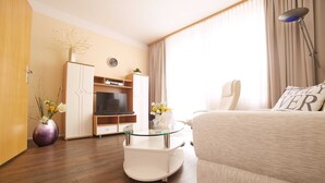 Ein modernes Hotelzimmer mit einer Couch, einem Glastisch, einem Fernseher, einem Kleiderschrank und einer Blumenvase.