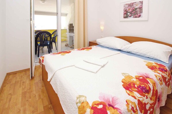 A bedroom with a bed, a nightstand, a chair, and a door leading to a balcony.