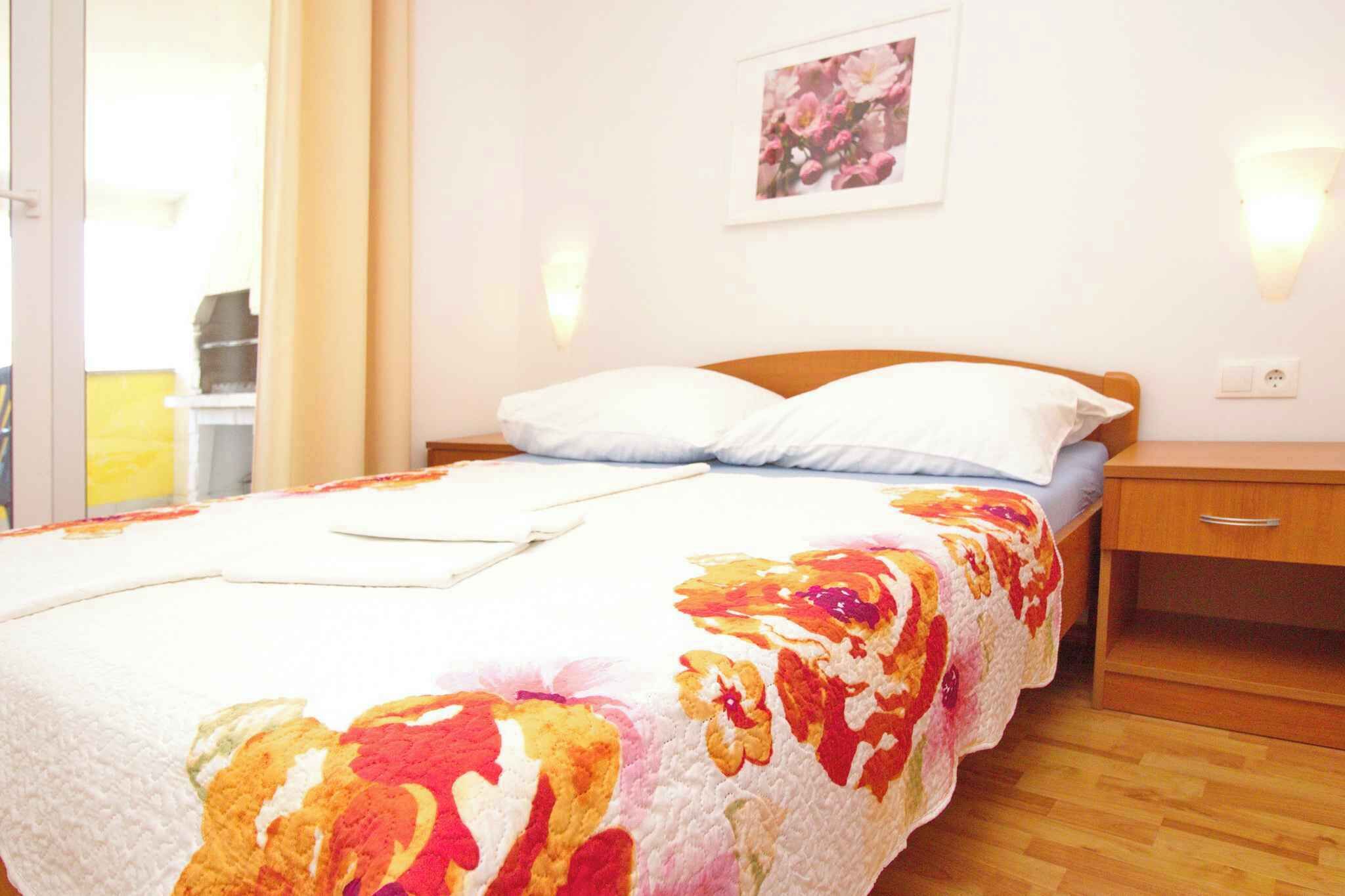 Un dormitorio con cama, mesita de noche, cajón de madera, lámpara de pared e imagen enmarcada.