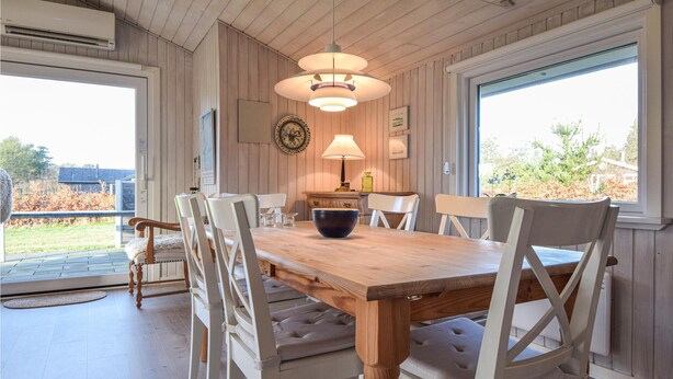 Un comedor con mesa de madera, sillas blancas tapizadas, una lámpara colgante y vistas al exterior.