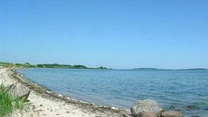 Une plage avec un ciel dégagé, une eau calme et une côte visible au loin.