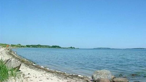Une plage avec un ciel dégagé, une eau calme et une côte visible au loin.