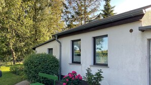 Un bâtiment à la façade blanche, un banc vert et des fleurs roses dans le jardin.