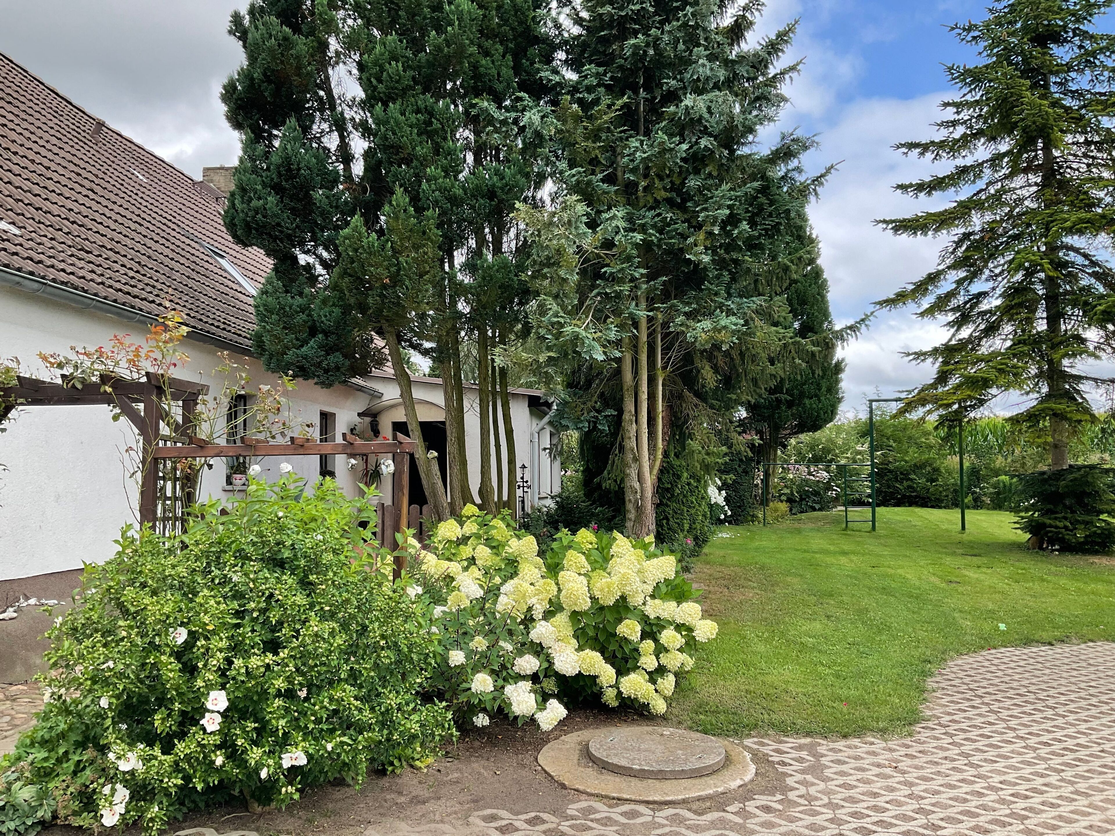 Un jardín con una casa blanca, árboles verdes y un césped.