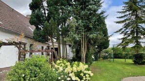Un jardin avec une maison blanche, des arbres verts et une pelouse verdoyante.