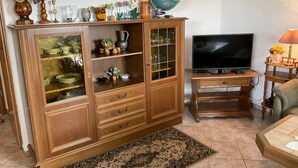 Un meuble en bois avec des portes en verre, un téléviseur posé sur un support en bois et une petite table avec une lampe.