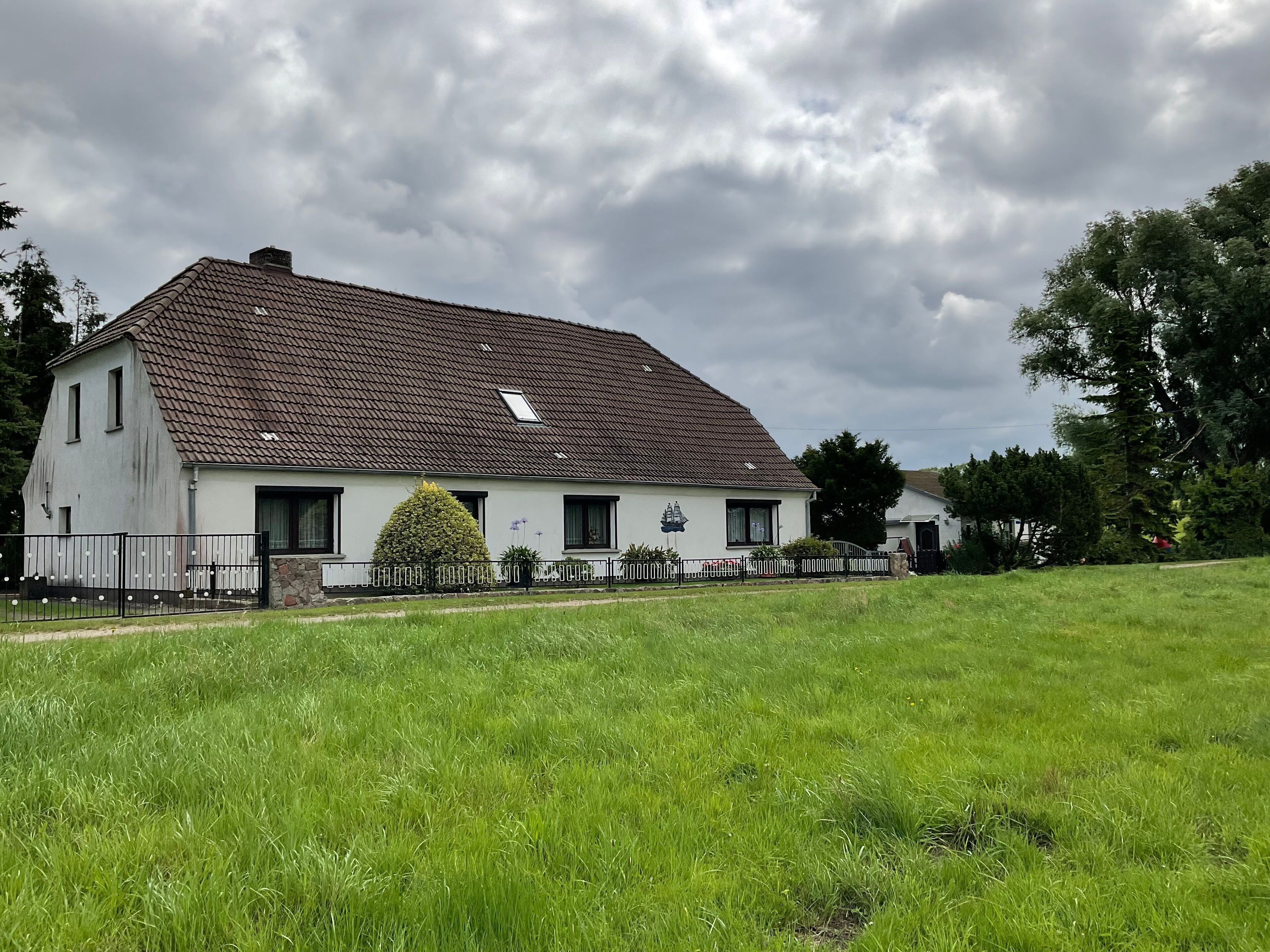 A two-story house with a sloped roof, a small garden, and a paved driveway.