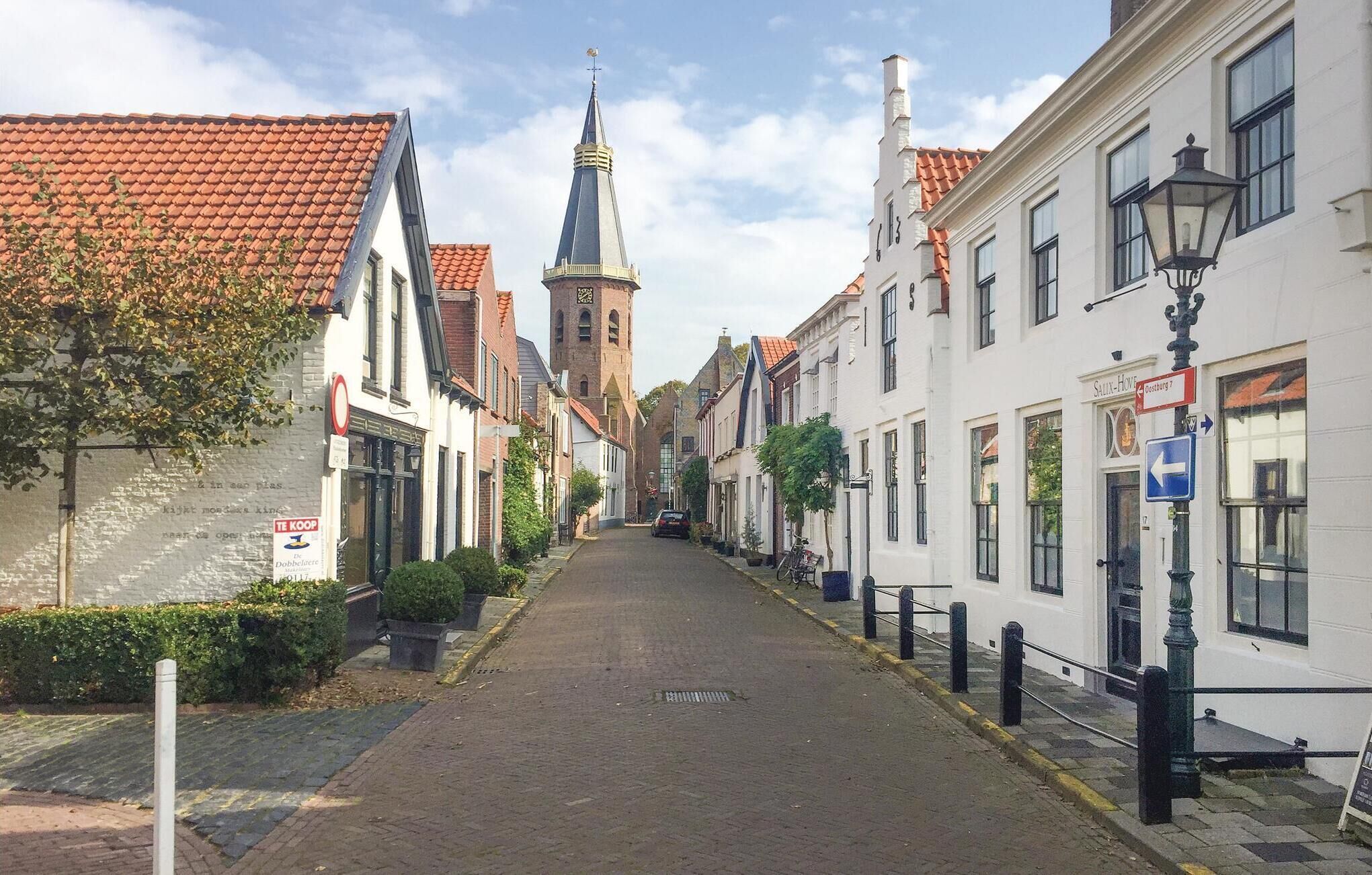 A narrow street lined with traditional European buildings, including a church with a tall spire.
