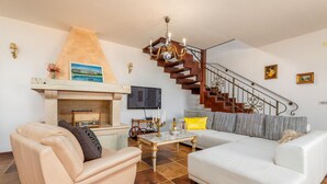 Un salon avec une cheminée, un canapé, une télévision et un escalier.