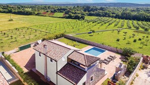 Une villa avec piscine, un patio doté de chaises longues et une vue sur la campagne environnante.