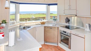Una cocina con vista al mar, un fregadero, lavavajillas, horno y hervidor.
