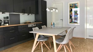 Een moderne keuken met donkere kastjes, een houten aanrecht en een eettafel met stoelen.