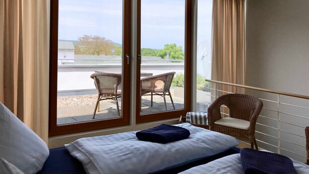 Een slaapkamer met een bed, uitzicht op een balkon en een stoel erbuiten.