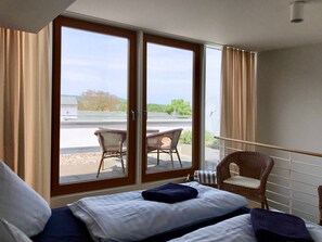 Ein Schlafzimmer mit Bett, Balkonblick und einem Stuhl davor.