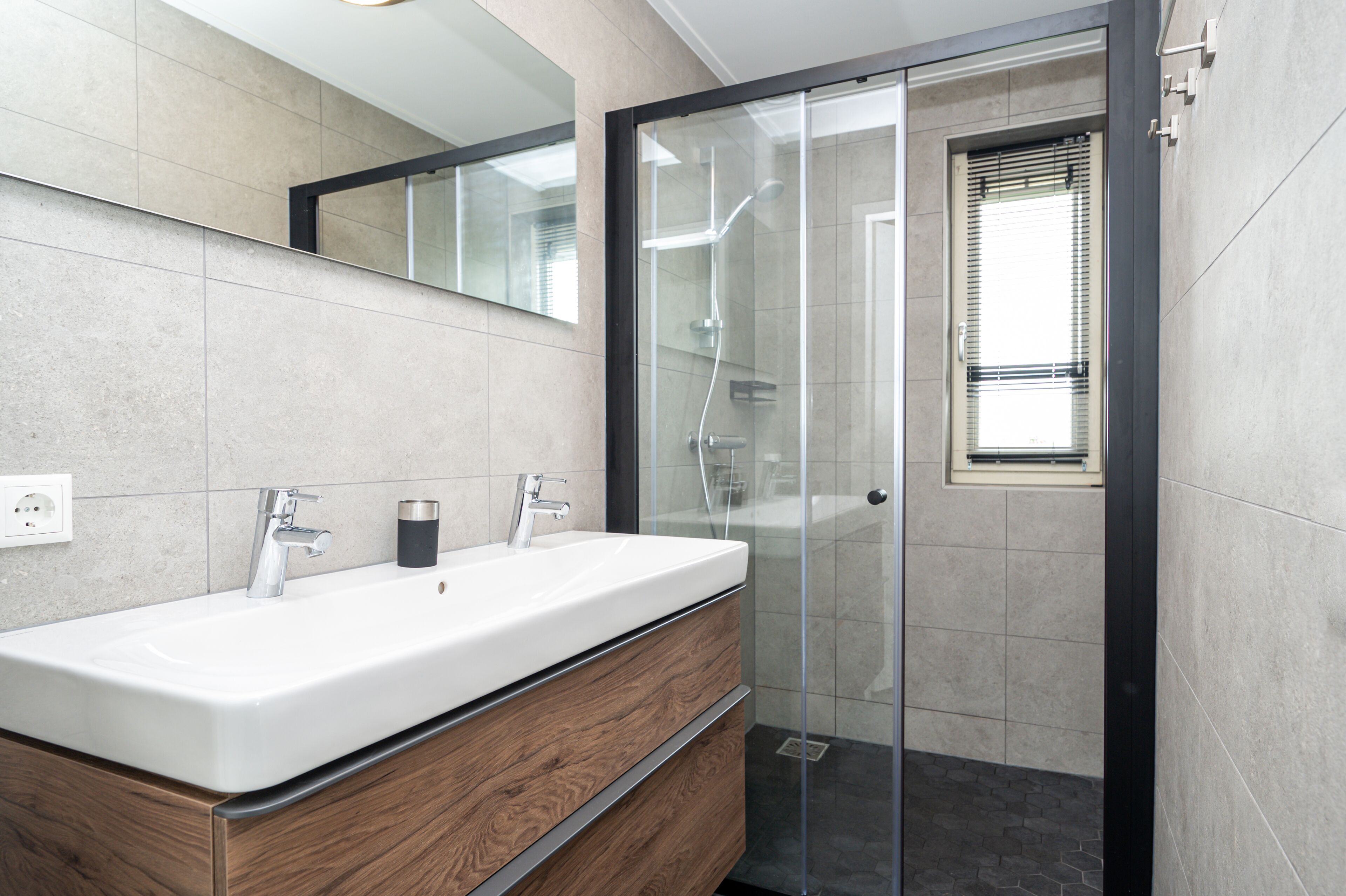 Ein modernes Badezimmer mit einem großen weißen Waschbecken, einem Holz-Waschtisch und einer Duschkabine aus Glas.