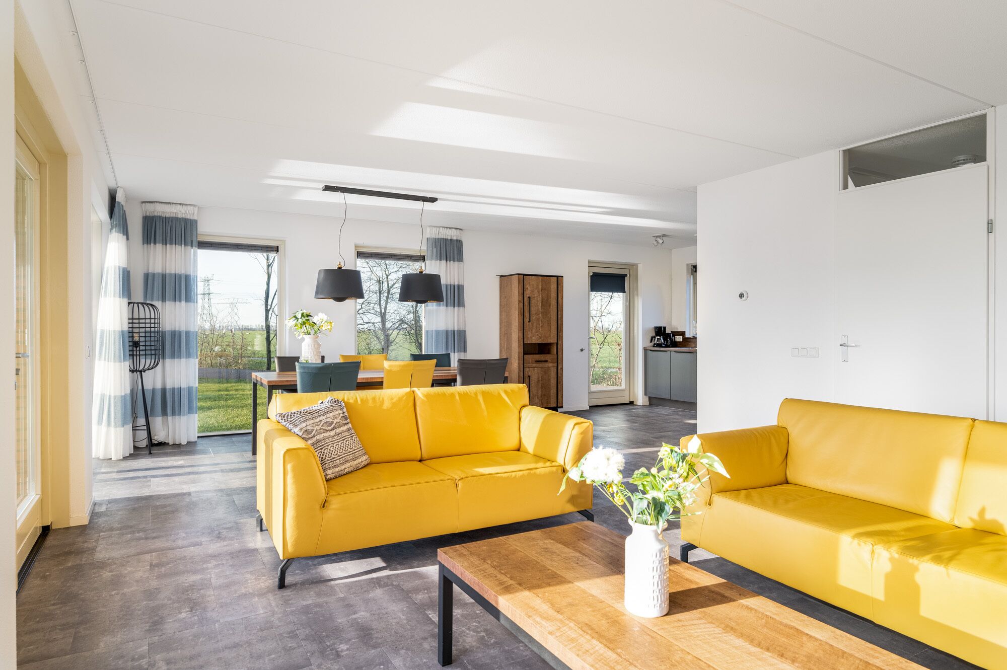 Una sala de estar moderna con un sofá amarillo, una mesa de centro de madera y vistas a la cocina y al comedor.