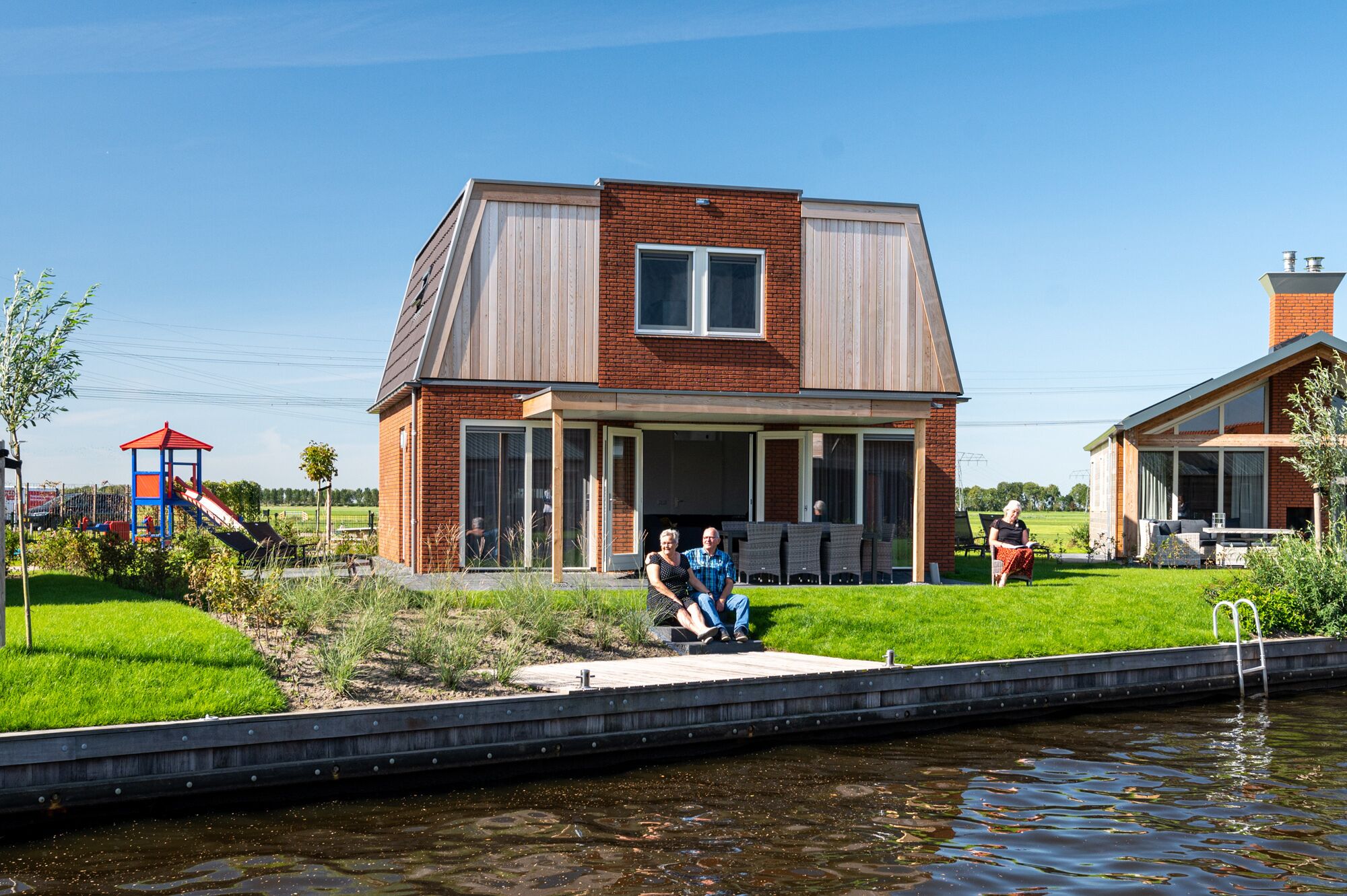 A modern house with a large window and a balcony, situated next to a body of water.