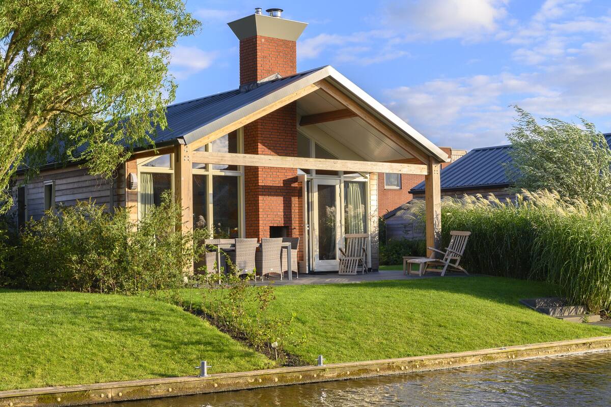 A house with a covered patio, a brick chimney, and a pond in the foreground.