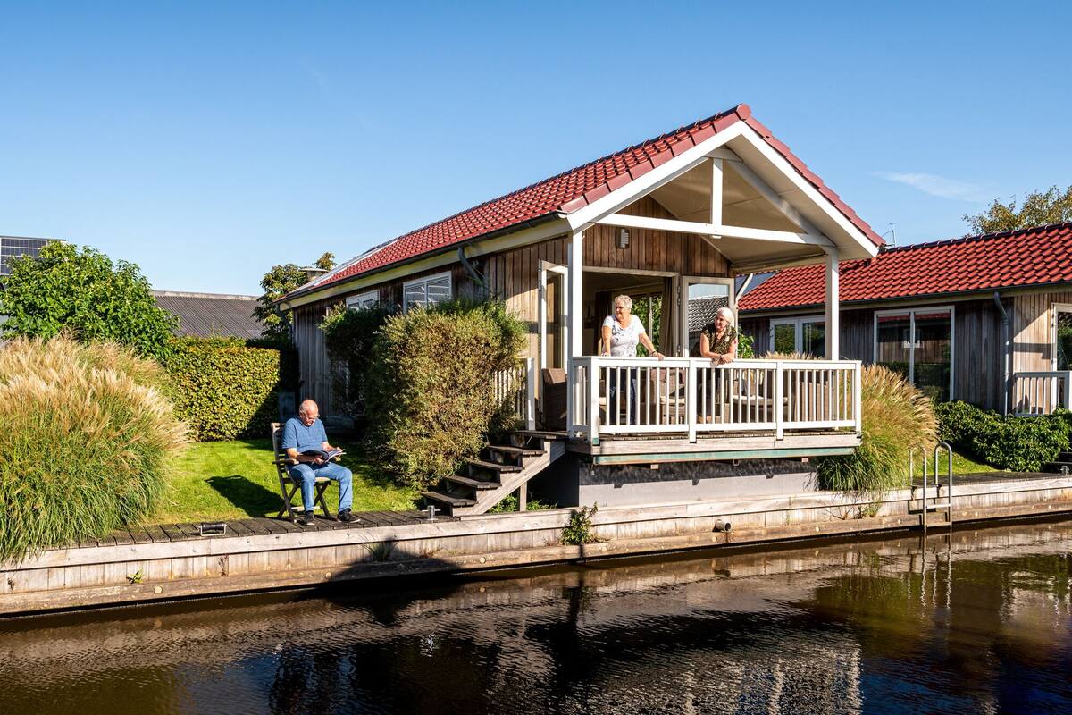 A wooden house with a red roof, a porch, and a small garden.
