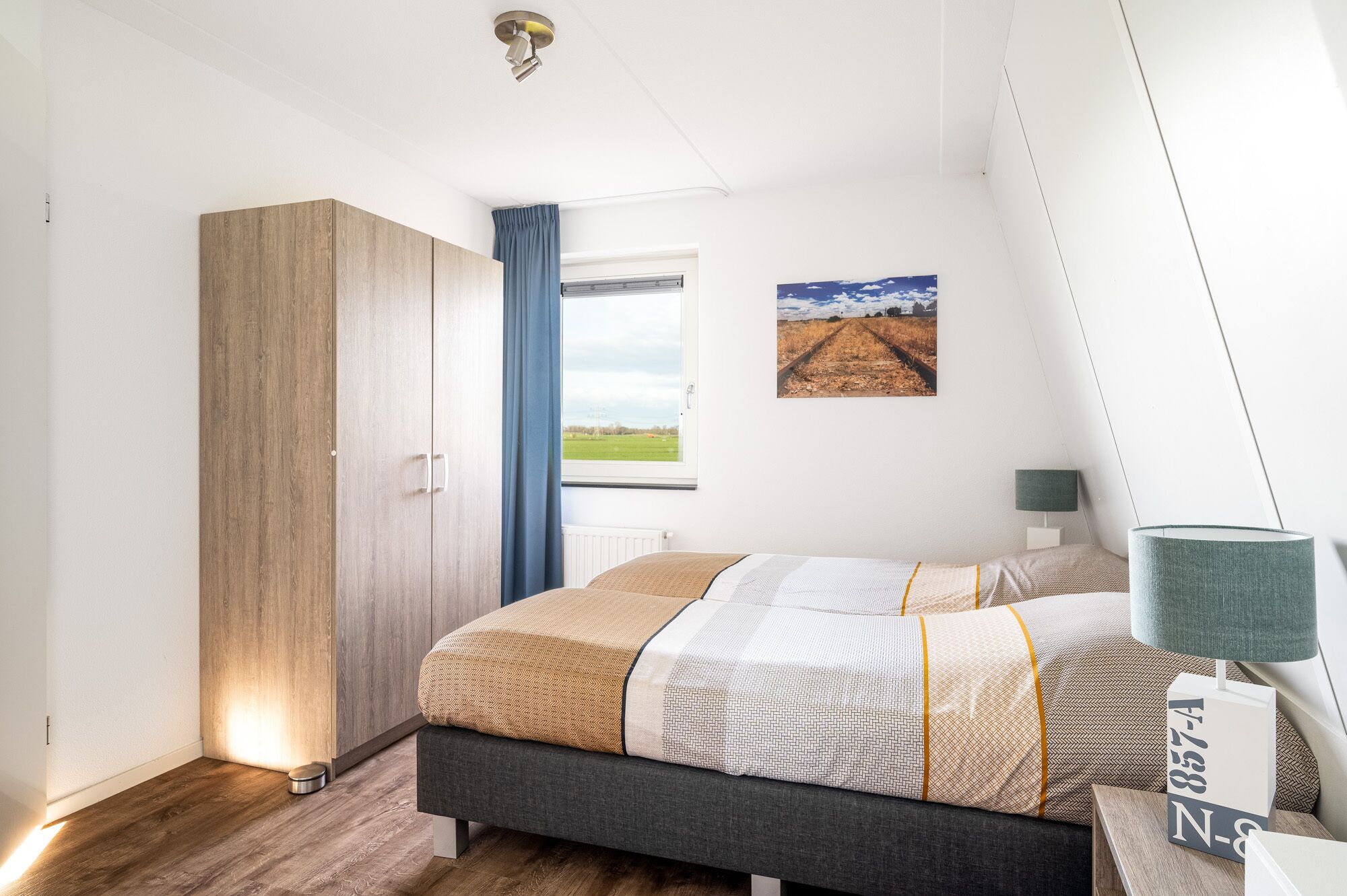 A bedroom with a bed, a wardrobe, a window with a view of a field, and a lamp.