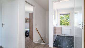 Un intérieur moderne avec un plancher en bois, des murs blancs et un hall d’entrée carrelé de noir.