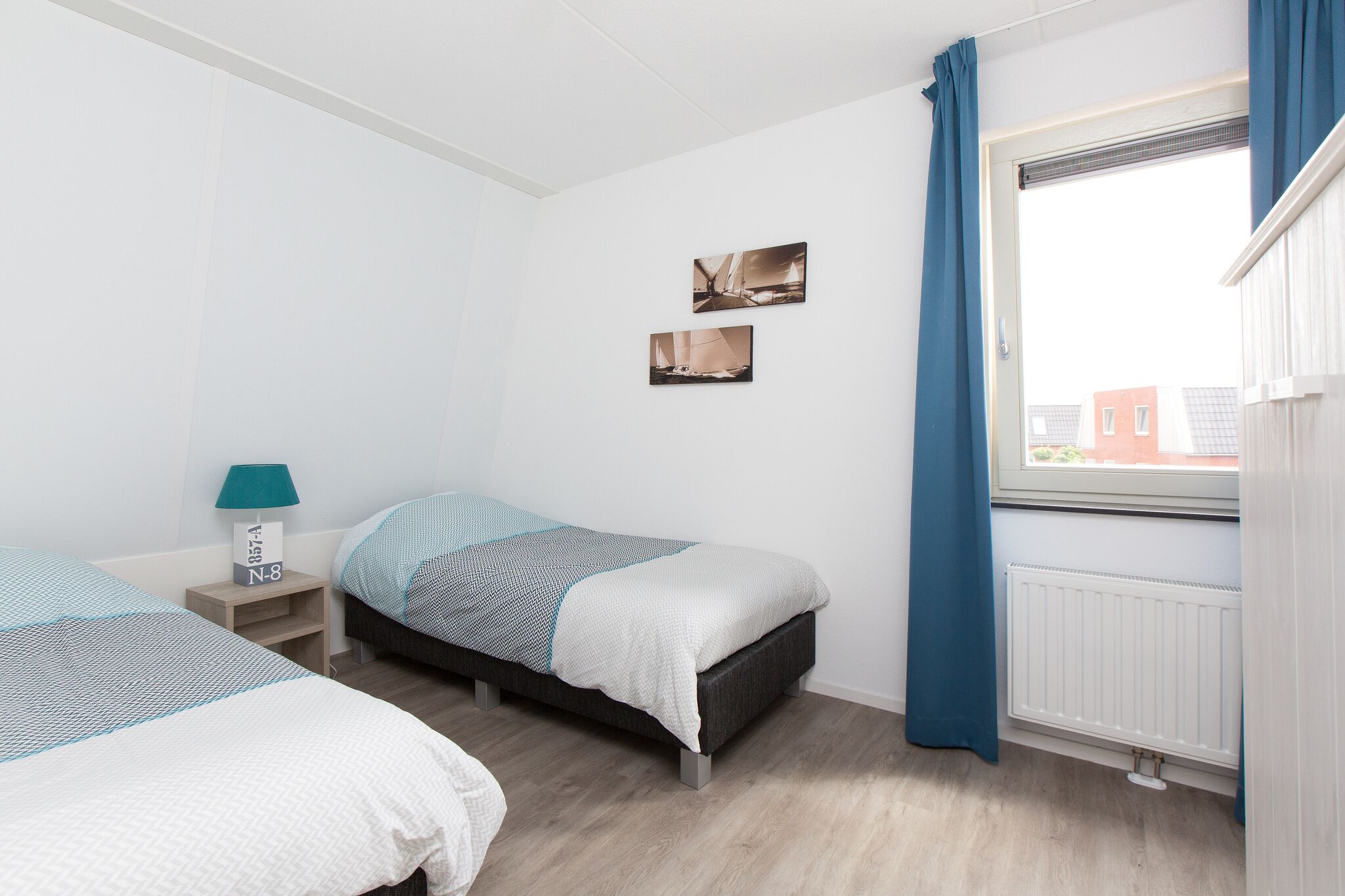 A bedroom with two beds, a nightstand, a window with curtains, and two wall-mounted pictures.