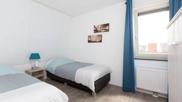 A bedroom with two beds, a nightstand, a window with curtains, and two wall-mounted pictures.