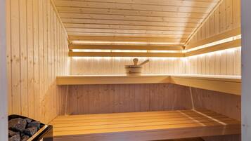 A sauna with wooden walls and benches, a stone bench on the left, and a wooden bench on the right.