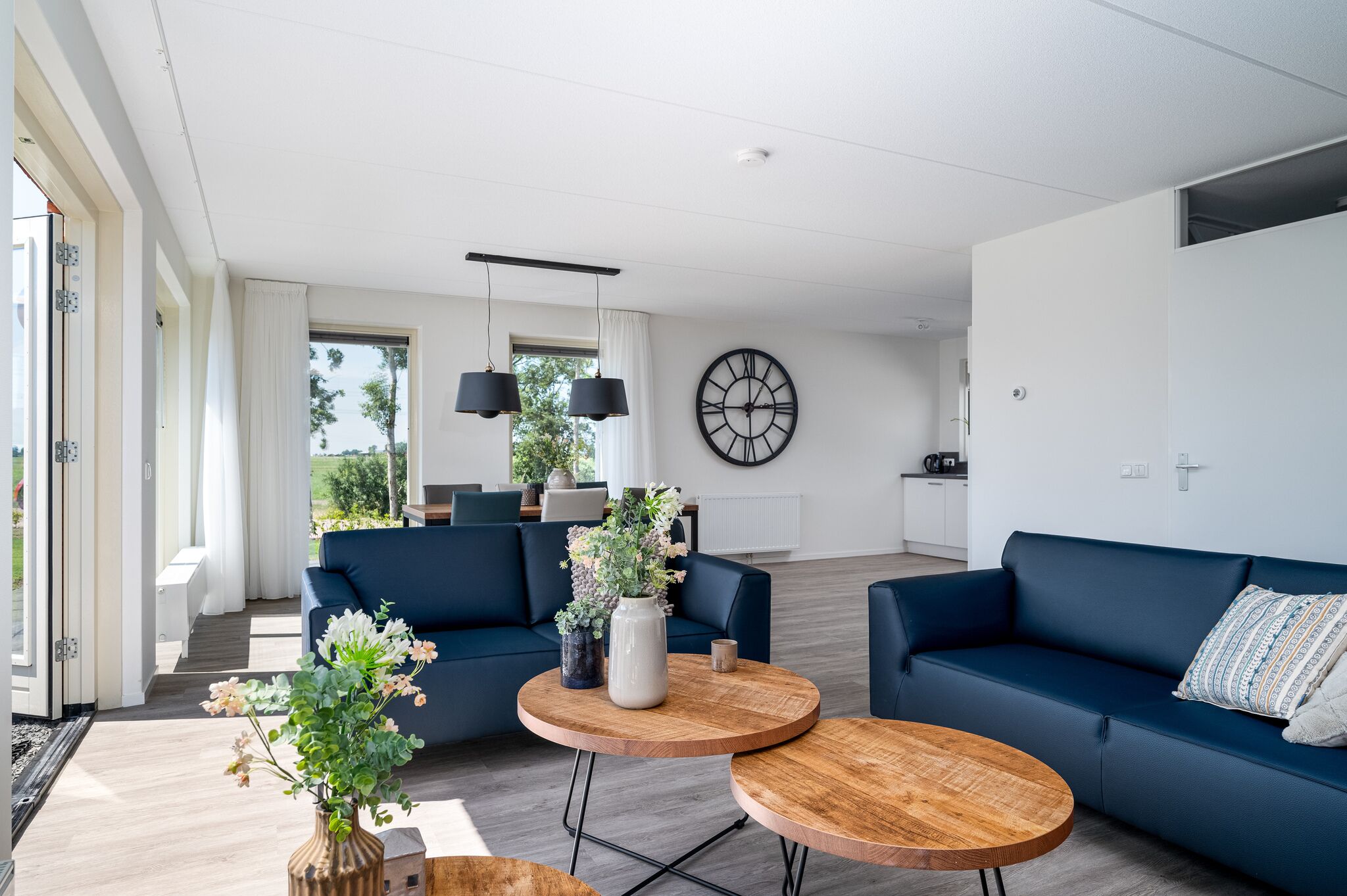 A modern living room with two dark blue sofas, a wooden coffee table, and a large wall clock.