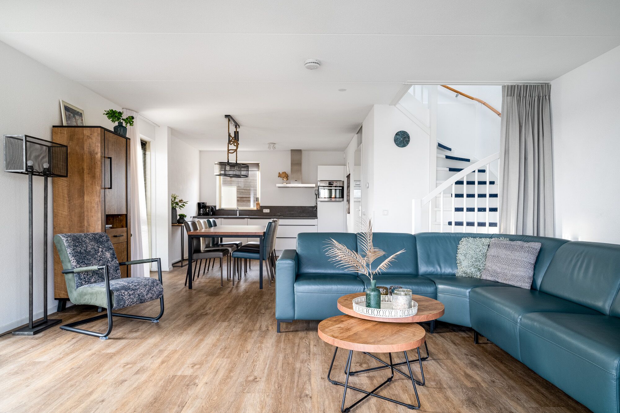 A modern living room with a blue sofa, a wooden coffee table, and a dining area with a kitchen in the background.