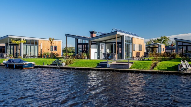 A modern waterfront property with a boat dock, large glass windows, and a well-maintained lawn. - Recreatiepark Tusken de Marren (Akkrum)
