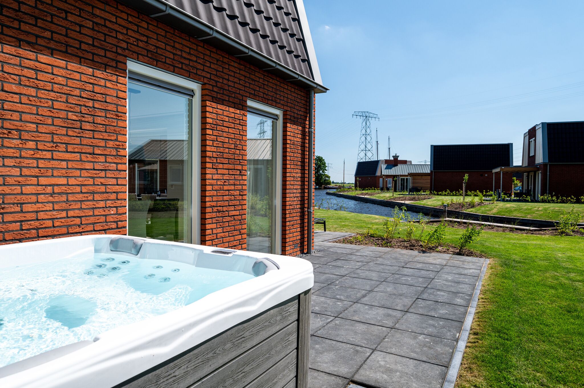 A modern house with a brick exterior, a hot tub, and a pathway leading to a canal.