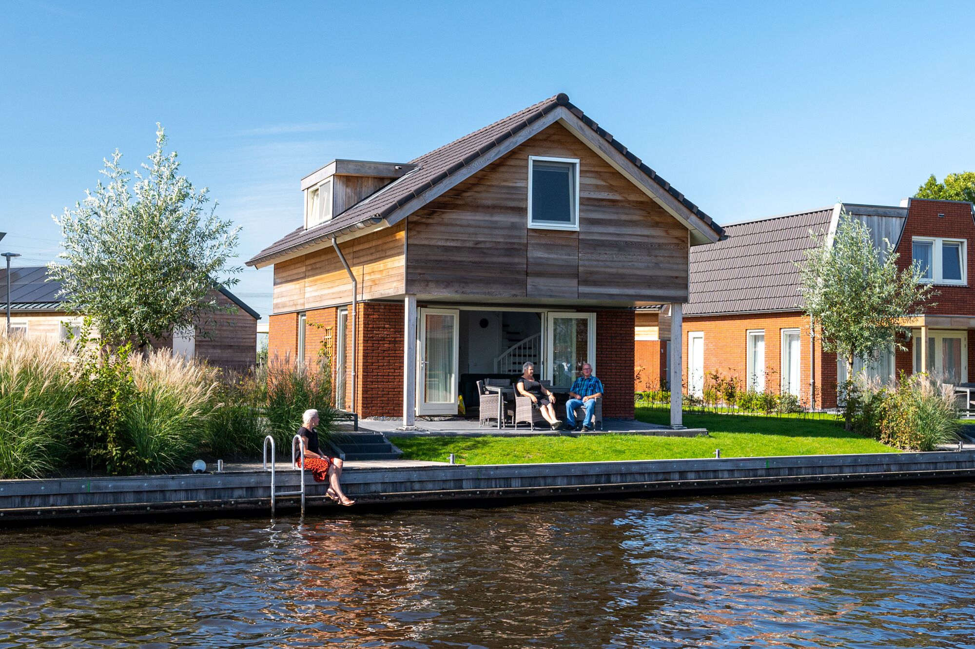 Una casa moderna con fachada de madera y un amplio ventanal, ubicada junto a un canal.