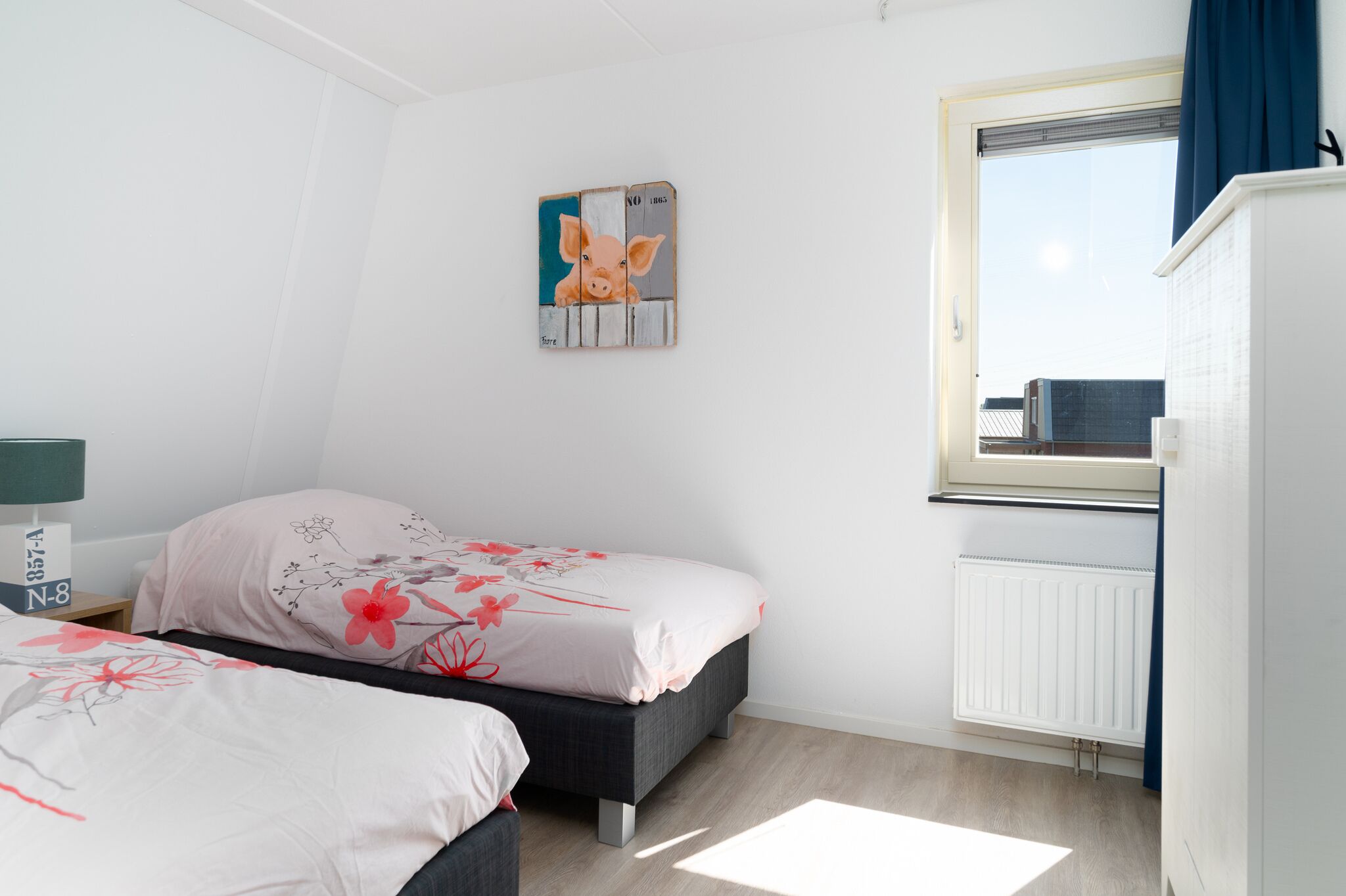 A bedroom with two beds, a window with a view, a radiator, and a wall-mounted artwork.