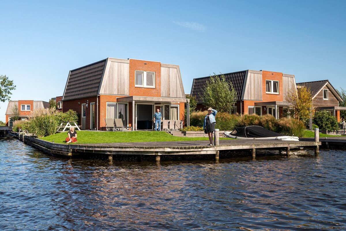 A canal-side house with a dock, a covered outdoor seating area, and a grassy front yard.
