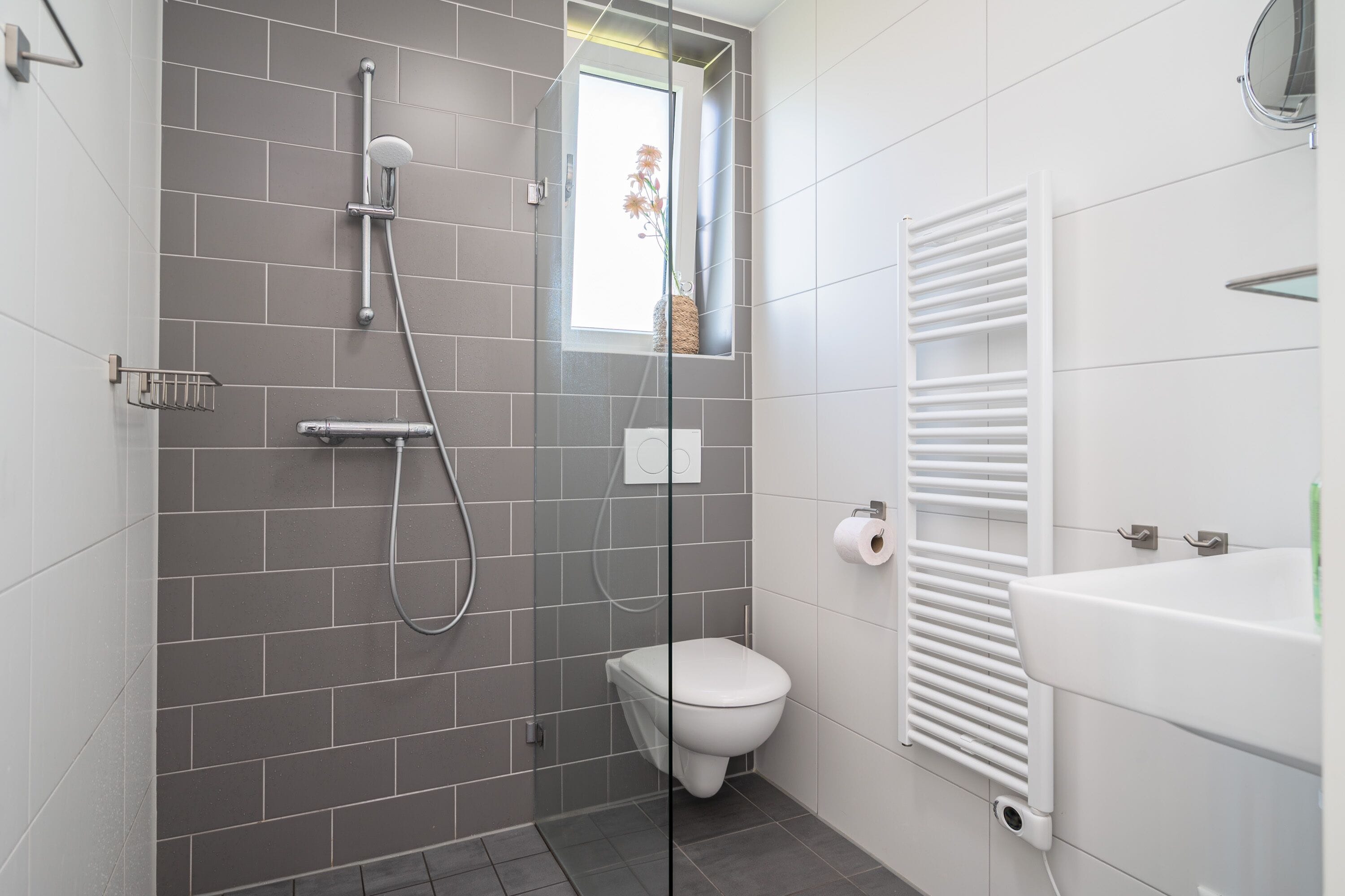 A modern bathroom with a glass-enclosed shower, a toilet, and a white bathtub.
