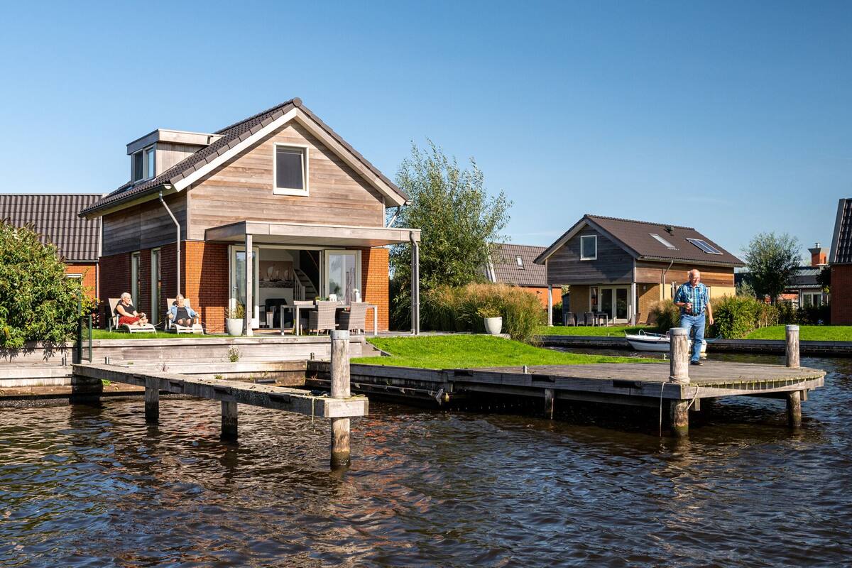 A riverside house with a dock extending into the water, a covered outdoor seating area, and a neighboring house.