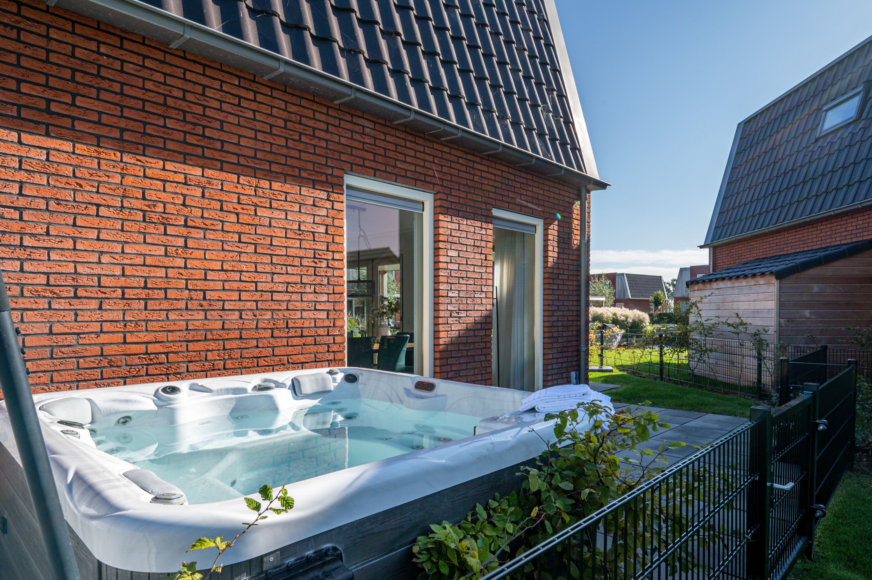 A brick house with a glass door and a hot tub in the backyard.