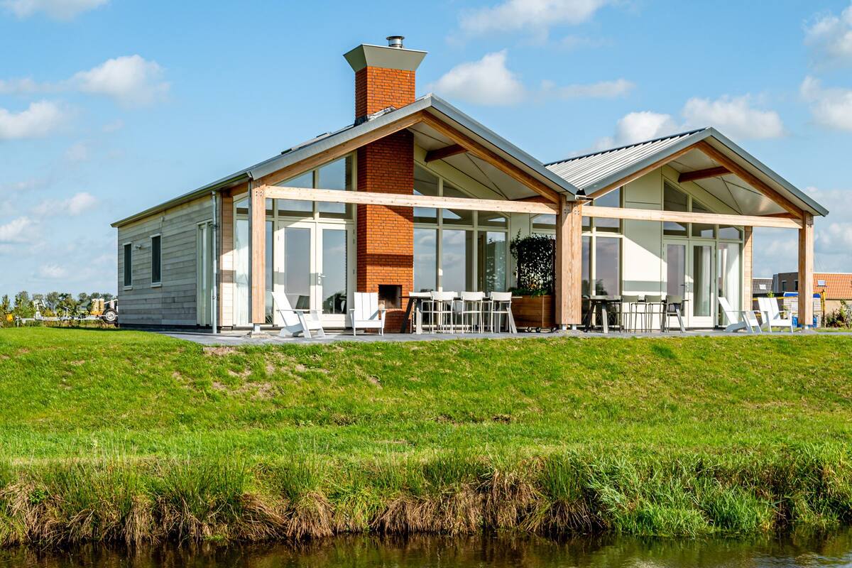 A modern house with a large glass front, a brick chimney, and a grassy lawn.