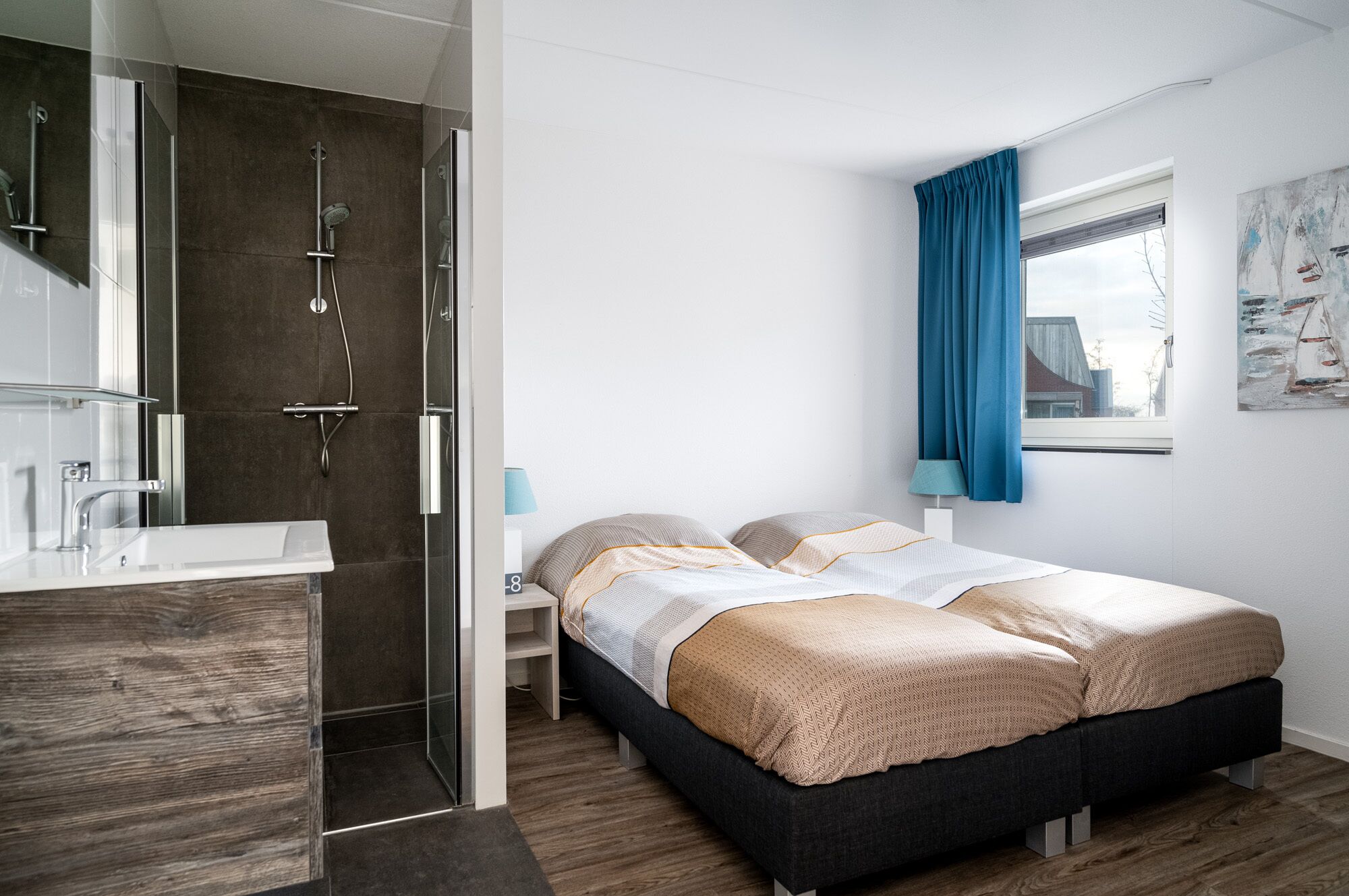 A modern bedroom with a bed, bedside tables, a window with curtains, and a bathroom with a shower.