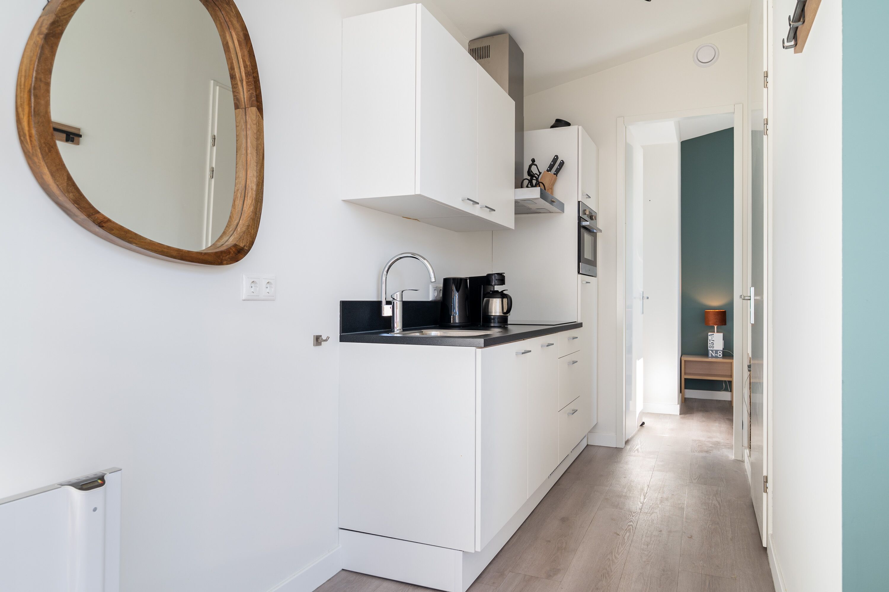 A modern kitchen with white cabinets, a black countertop, and a wooden-framed mirror.
