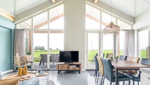 A spacious living room with a large TV, dining area, and a view of the outdoors. - Recreatiepark Tusken de Marren (Akkrum)