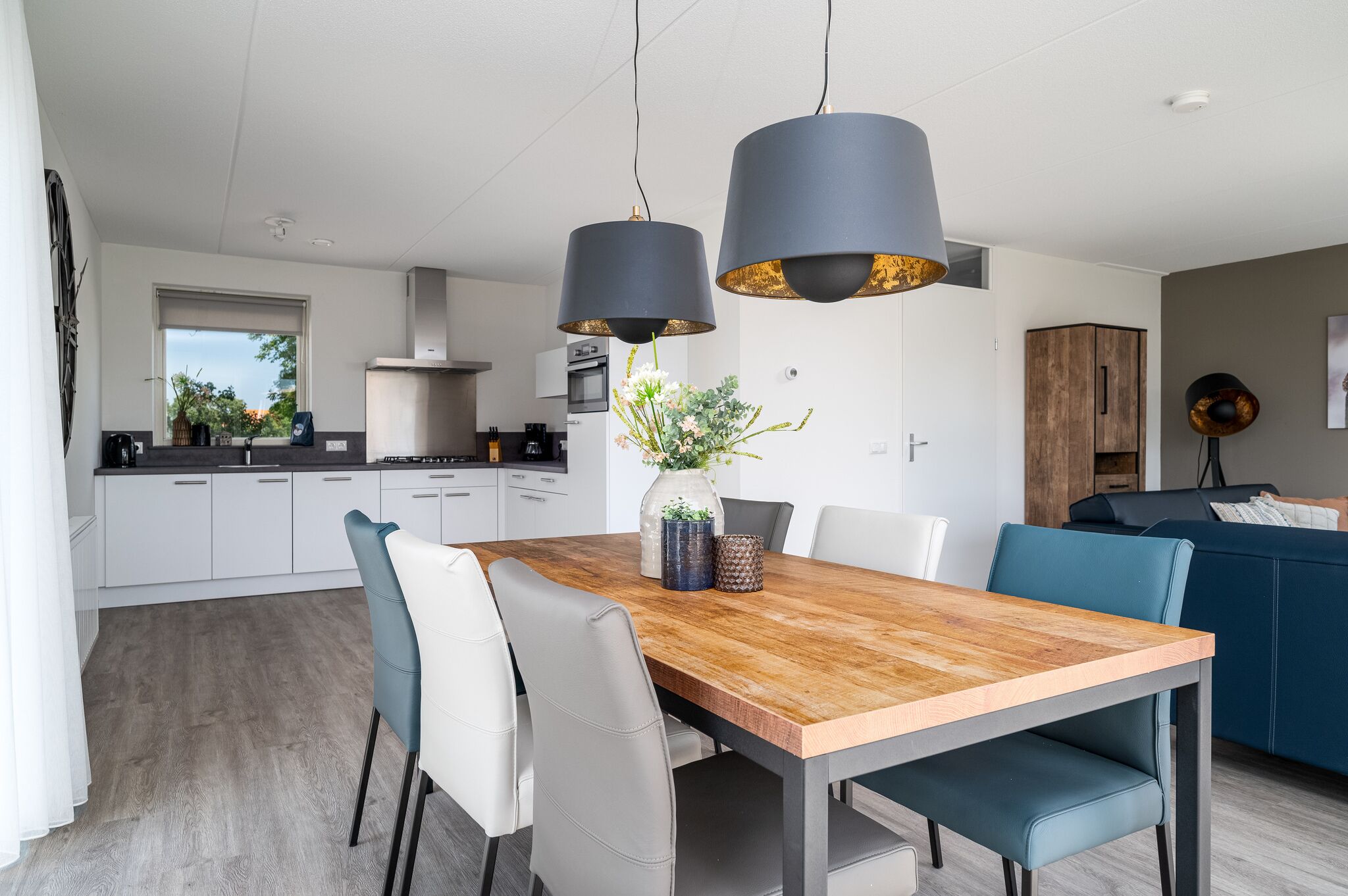 A modern kitchen with white cabinets, a wooden dining table, and two pendant lights.