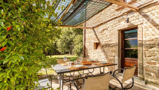 Un espace de restauration en plein air, avec un bâtiment en pierre, une table dressée pour deux personnes et une pergola au-dessus.