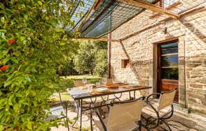 An outdoor dining area with a stone building, a table set for two, and a pergola overhead. - Pet friendly home in Cortona AR (Cortona AR)