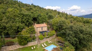 Une maison en pierre, avec un toit en tuiles, entourée d’une végétation luxuriante et dotée d’une piscine.